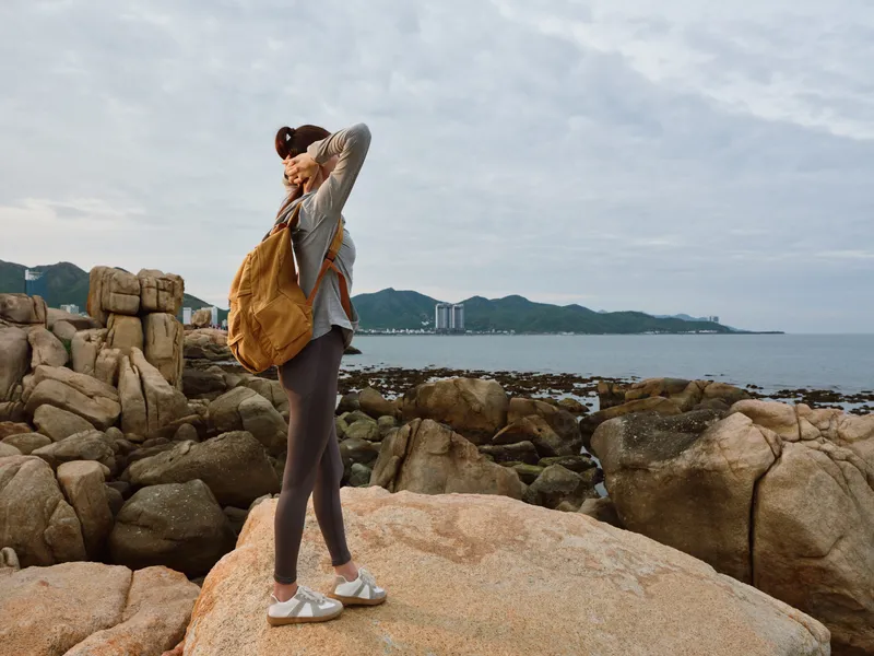 Young woman enjoying the scenic view at the rocky beach, dressed in casual sporty attire, conveying a sense of adventure and tranquility in nature