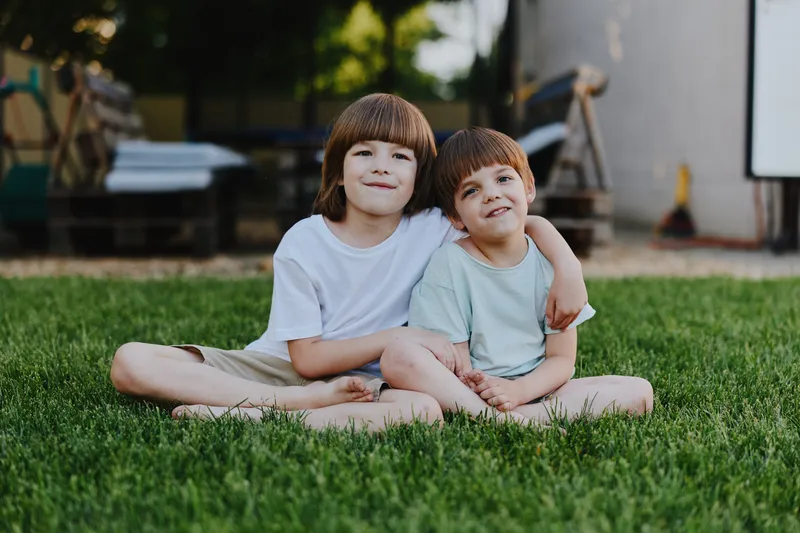 Two cheerful boys sitting together on green grass, enjoying a sunny day, showcasing friendship and childhood innocence in a playful atmosphere.