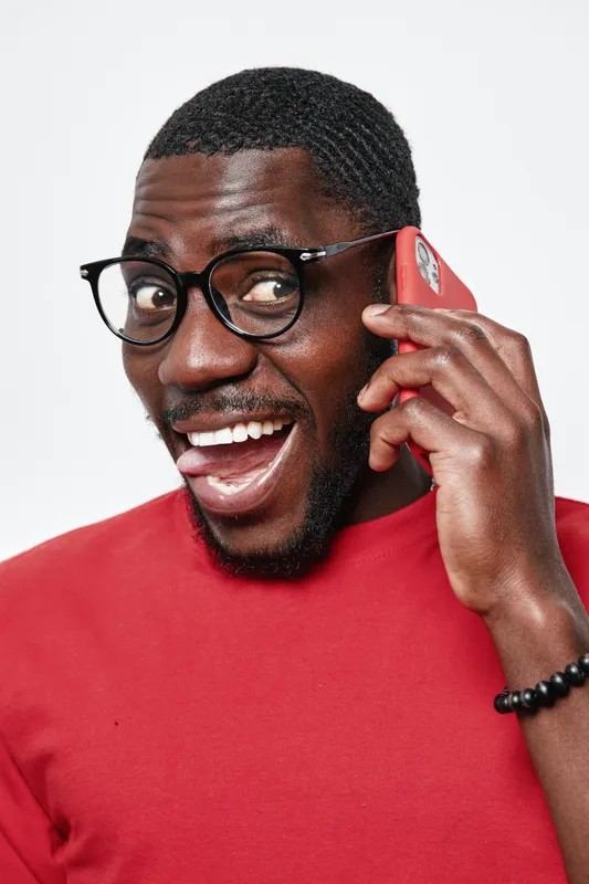 African American man with dark skin wearing glasses and red shirt talking on smartphone with happy expression isolated on white background. Communication, technology and lifestyle.
