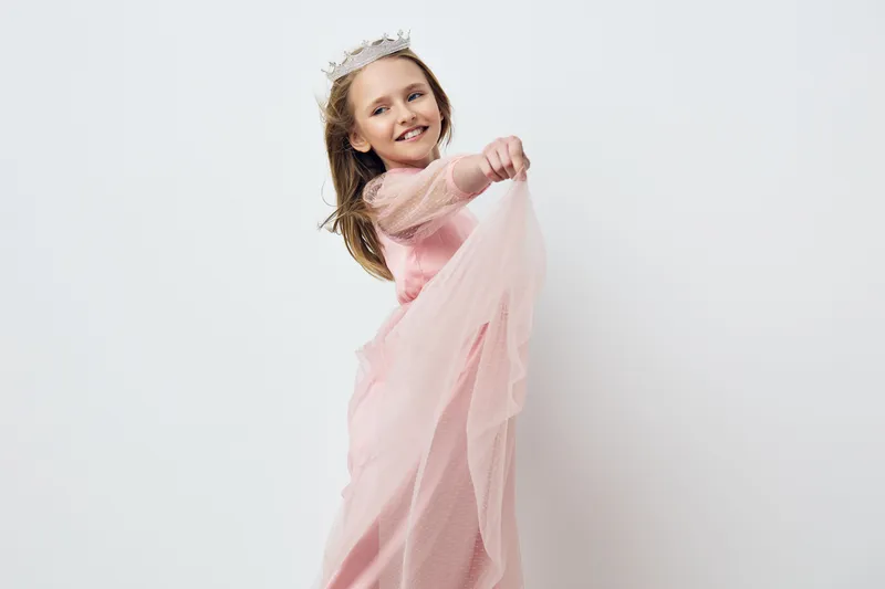 Young girl in a pink dress with a crown, joyfully twirling, exuding happiness and innocence in a minimalistic white background Ideal for children s fashion themes