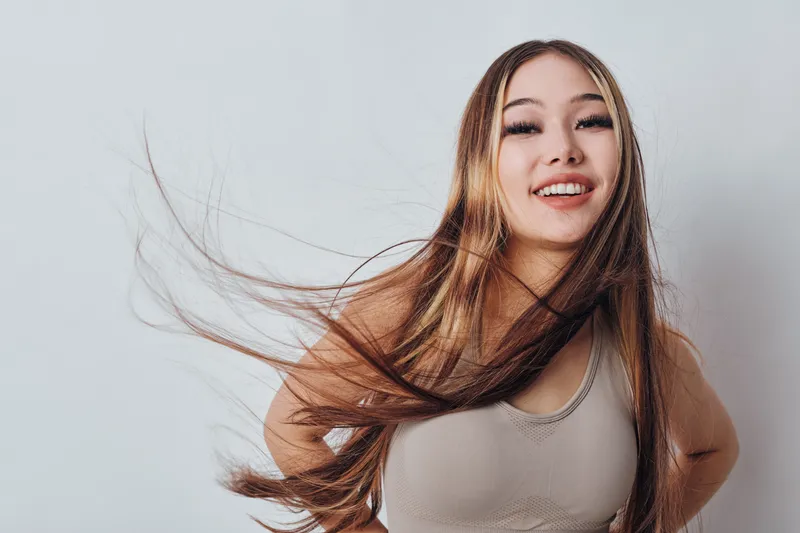Happy woman with long hair smiling and posing in studio wearing casual top isolated on white background. Female model expressing joy and confidence with natural makeup.