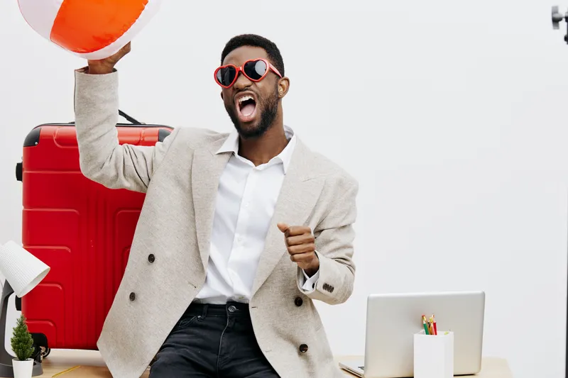 Joyful young man in sunglasses celebrating with a suitcase and beach ball, excited about travel plans. Casual style, upbeat mood, modern office background, vibrant colors, summer vibe, lifestyle conce