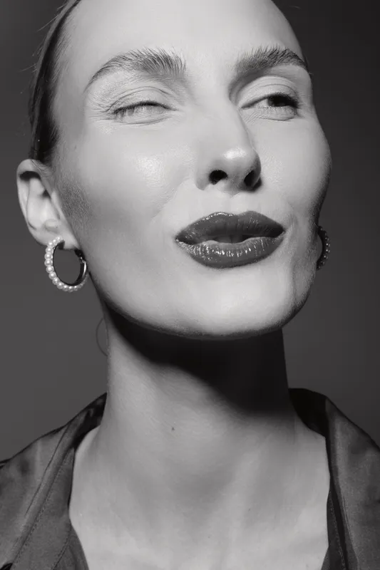 Close-up of a pale white woman with smooth skin and pearl earrings winking and puckering lips in a studio. Concept of beauty and expression.