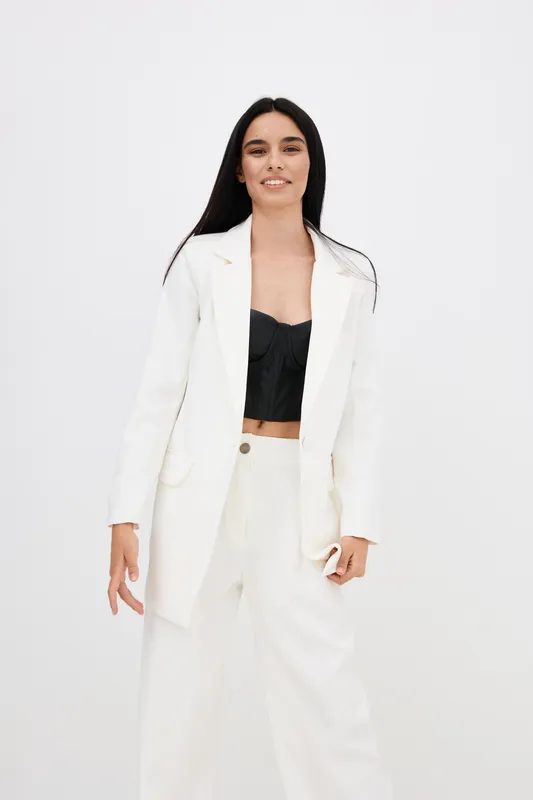 confident woman in white suit and black top standing with relaxed posture against plain white background, showcasing modern fashion style and natural smile