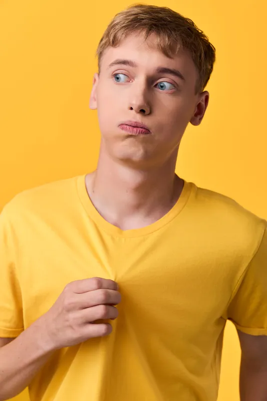 Confused expression of a man in a yellow shirt against a bright yellow studio backdrop, looking to the side, portraying curiosity, fashion, and creative mood.