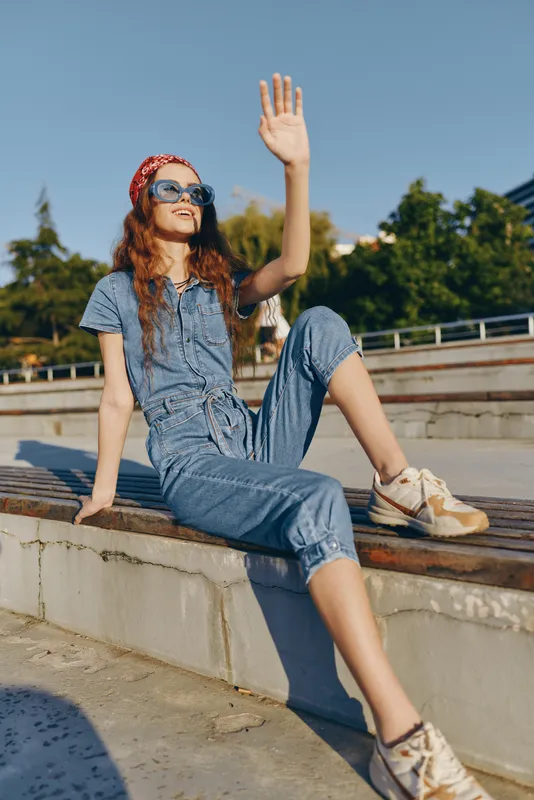 lifestyle woman in modern boho-western denim street style wearing sunglasses and red bandana, sitting outdoors with film color effect, sunlit setting with casual vibe