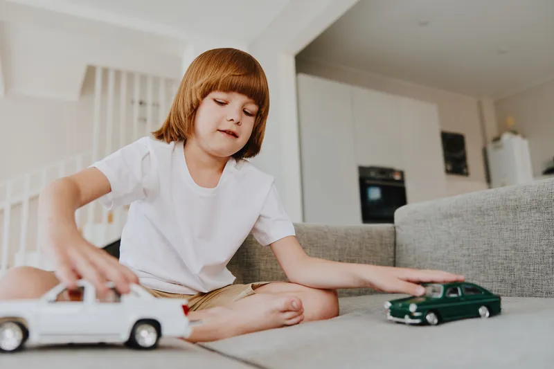 Happy boy playing with toy cars indoors, engaged in imaginative play. Bright and cozy setting enhances the warmth of childhood moments.
