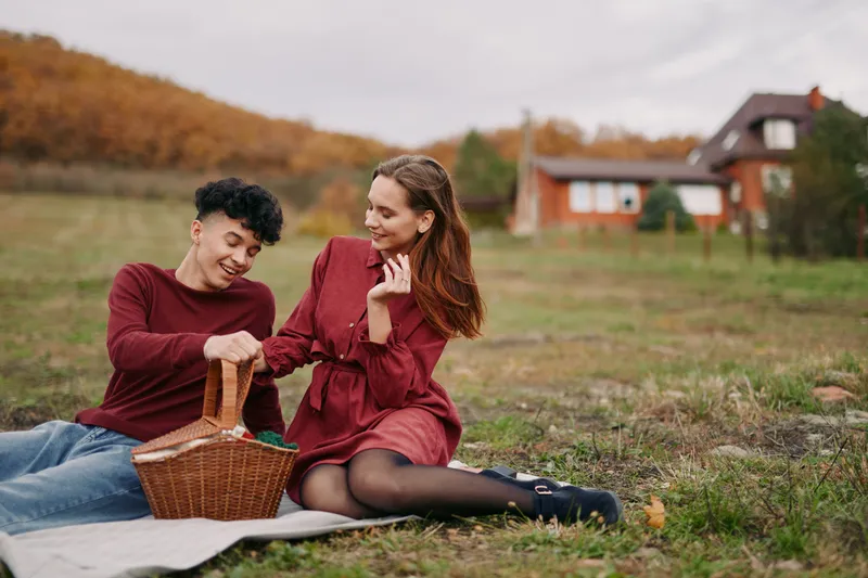 A candid moment of a couple picnicking in a sunlit field, radiating authenticity and warmth as they share a smile and simple joy on a relaxed afternoon.