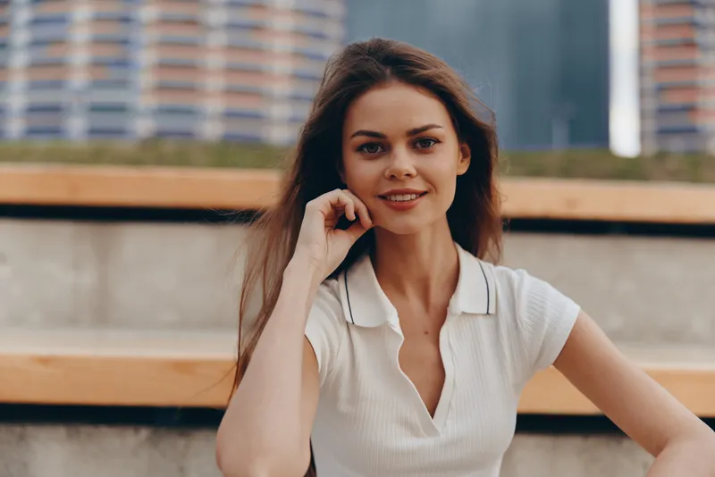 Young woman in casual white polo shirt smiling outdoors with urban background, natural light, relaxed confident expression, summer lifestyle portrait