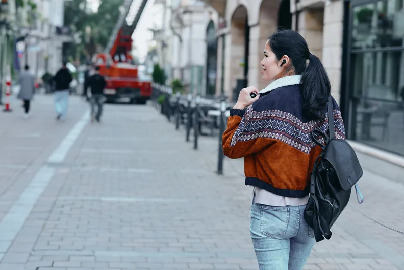 Walking woman with a backpack along a quiet urban street, casual fashion and street style, city sidewalk and storefronts, autumn colors and candid vibe for lifestyle and travel photography