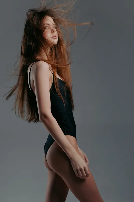 young woman in black swimsuit with flowing hair against gray background