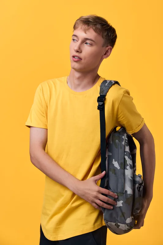 Youth, casual style in a yellow shirt and camouflage backpack for school and everyday wear, bright studio setup, streetwear inspired vibe, confident expression and relaxed pose
