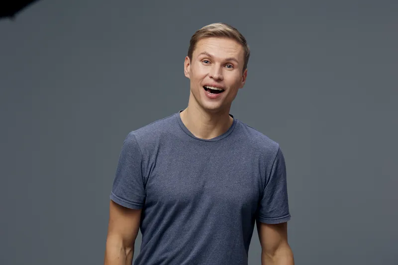 Smiling man wearing casual blue t-shirt looking at camera with cheerful expression on plain gray background studio portrait. People lifestyle concept
