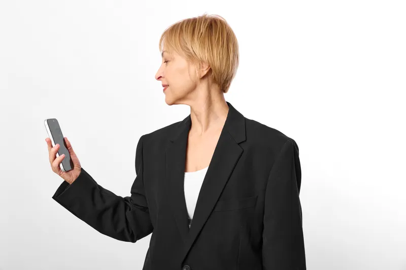 Businesswoman smartphone technology communication portrait gesture blonde blazer, woman holds phone and shows screen, confident view, office white background