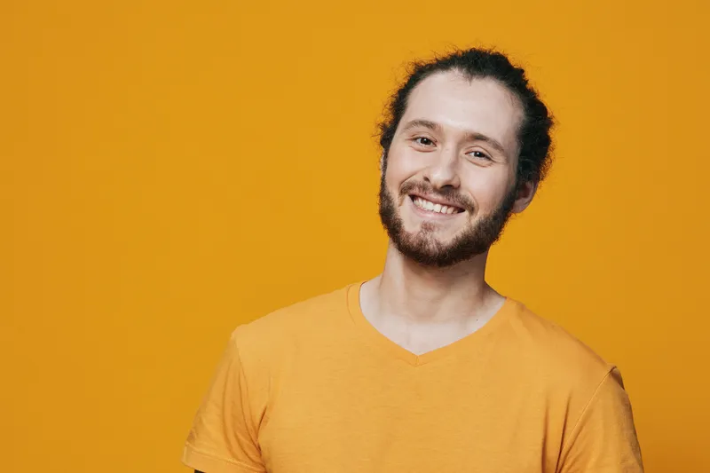Cheerful young man with curly hair smiling in a bright yellow t shirt against a vibrant yellow background, embodying positivity and joy