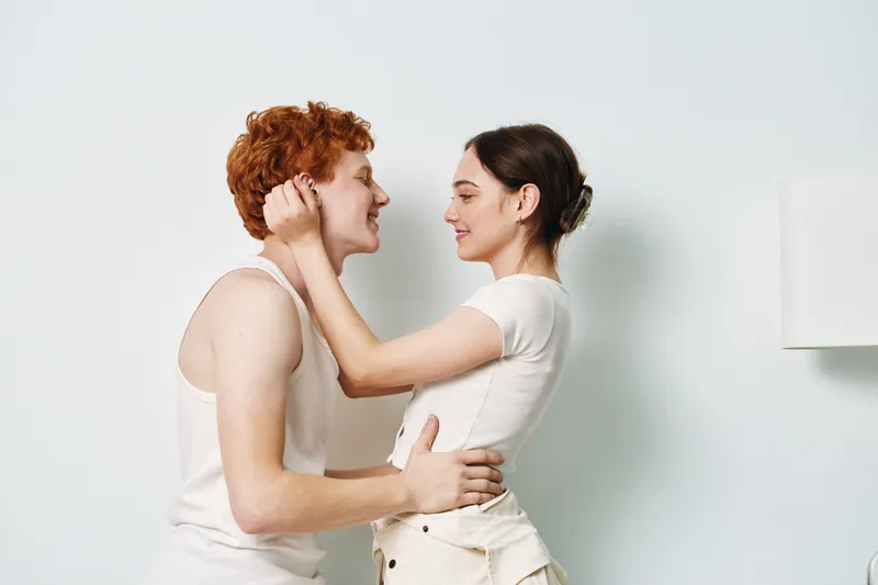 Couple embracing indoors with tenderness and love, smiling young man and woman in casual clothes sharing intimate moment in bright room with minimalist decor.