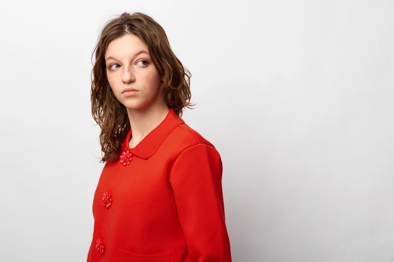 Young woman in red sweater looks sideways with a thoughtful expression. Isolated on white background. Concept of contemplation, emotion, and casual fashion portrait.