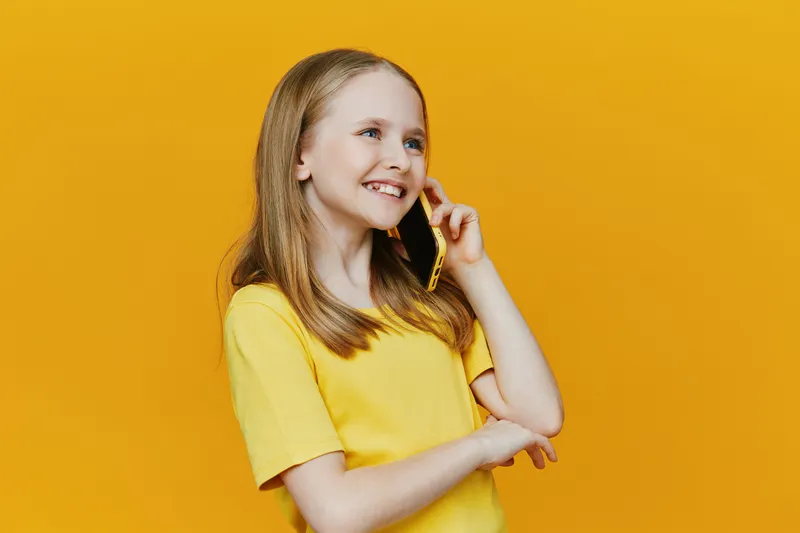 Happy girl talking on the phone against a vibrant yellow background, wearing a casual yellow t shirt, showcasing joy and connection in a playful concept