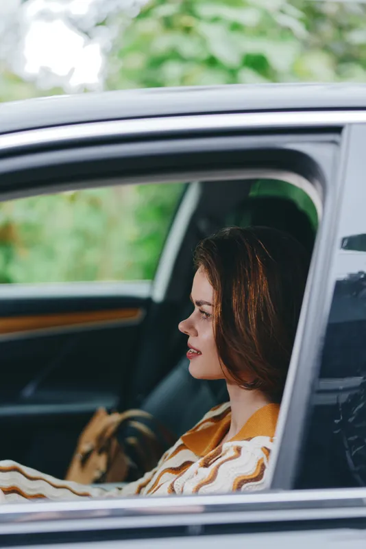 Woman sits in a car, profile view by the window, calm expression and soft natural light highlighting the interior.