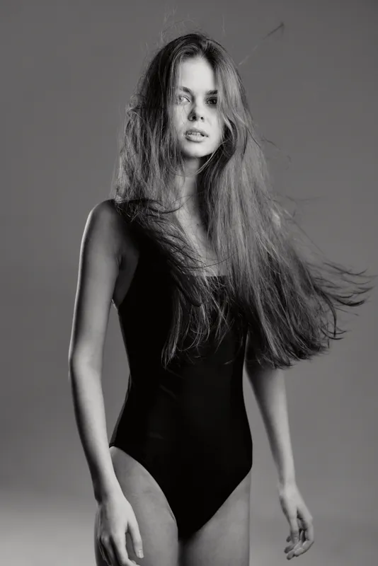 Black and white portrait of a young woman with long hair wearing a black swimsuit, showing natural beauty and elegance.