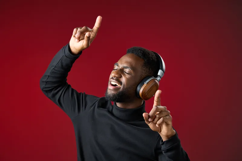 Happy young man dancing with headphones in a stylish black outfit against a vibrant red background, expressing joy and music enjoyment