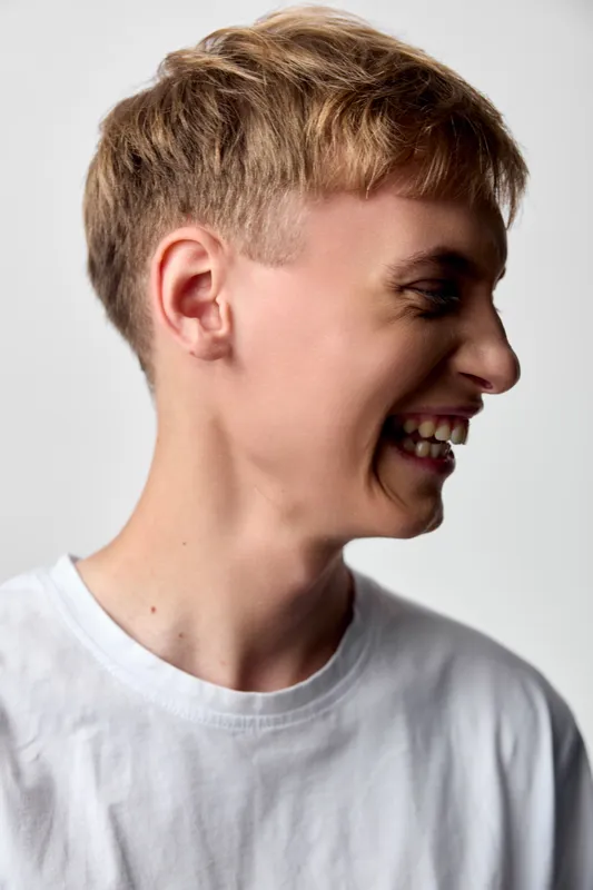 Smiling boy, laughing face, joyful expression, casual white shirt, youth happiness, candid moment, playful mood, studio lighting, head turn, cheerful energy, showcasing carefree youth and bright