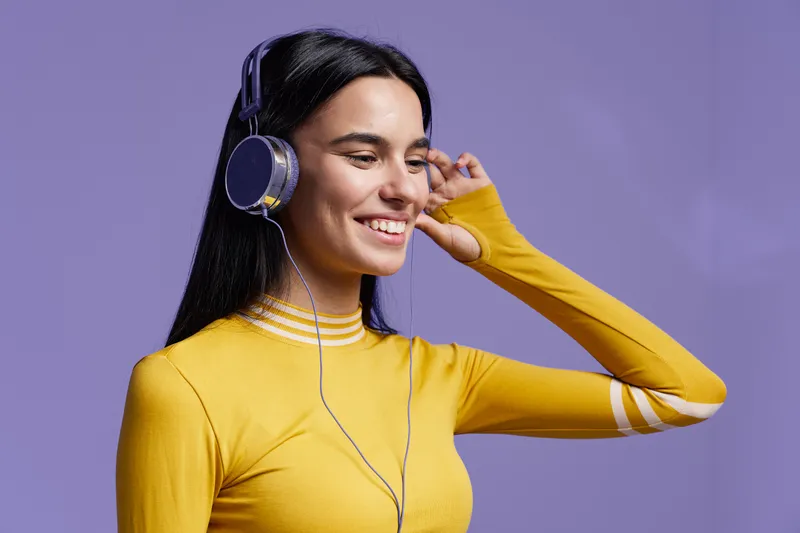 happy woman sport fitness wearing yellow top and headphones, enjoying music with bright purple background, positive energy and healthy lifestyle concept