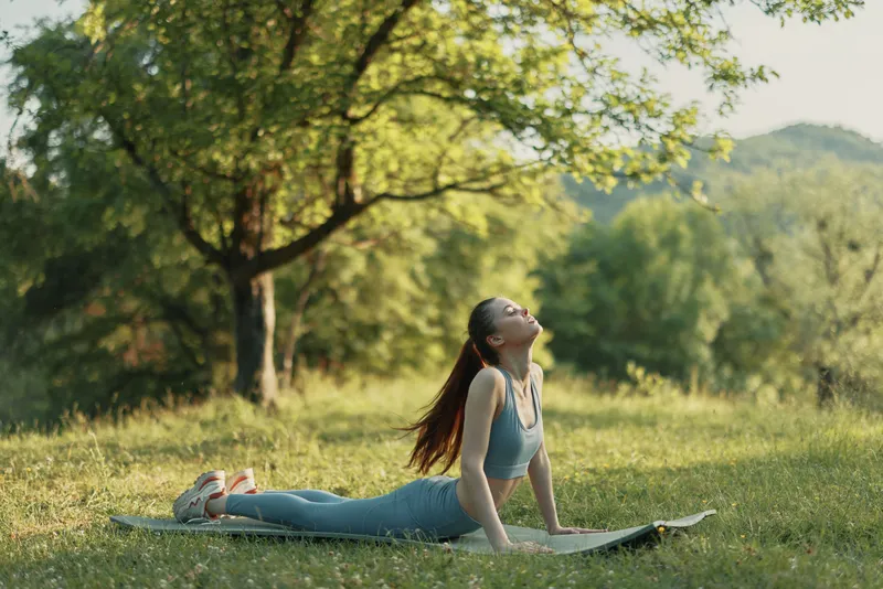 Young woman practicing yoga in a serene green park, wearing activewear, exhibiting a peaceful expression, surrounded by nature