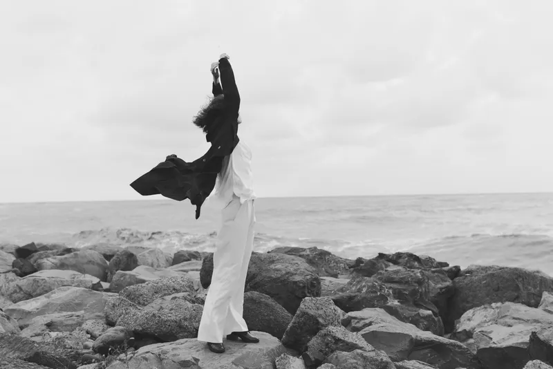 Couple dancing on rugged rocks by the sea, wind lifting their garments as they embrace and move, monochrome scene capturing motion, romance, and freedom against a timeless horizon