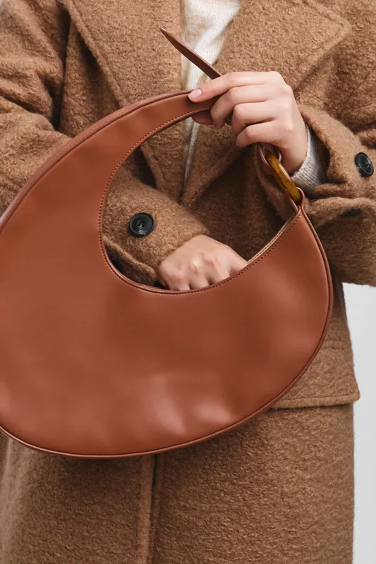 asian woman carries a chic leather handbag in a stylish outerwear look, posing against a clean urban backdrop with a contemporary fashion vibe.
