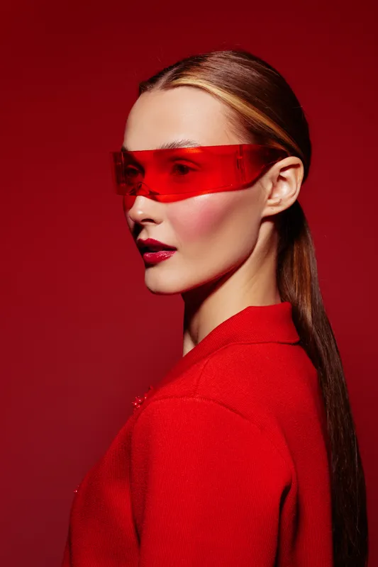 Profile of a young woman wearing red futuristic sunglasses and a red outfit against a red background. Concept of fashion, style, and modern accessories.