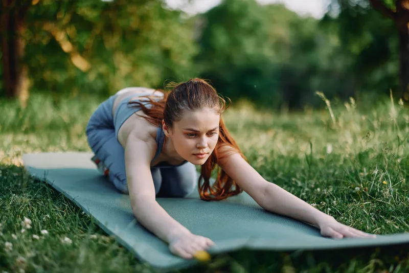 Young woman practicing yoga on a mat in a serene green park, showcasing mindfulness and relaxation during a sunny day
