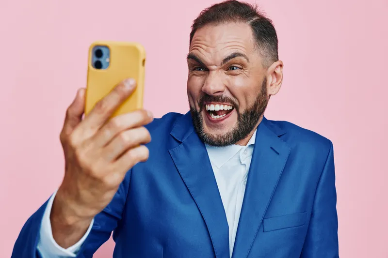 A confident business professional captures a vibrant selfie against a solid pink background, showcasing energy, enthusiasm, and a bold, upbeat mood in a modern setting.