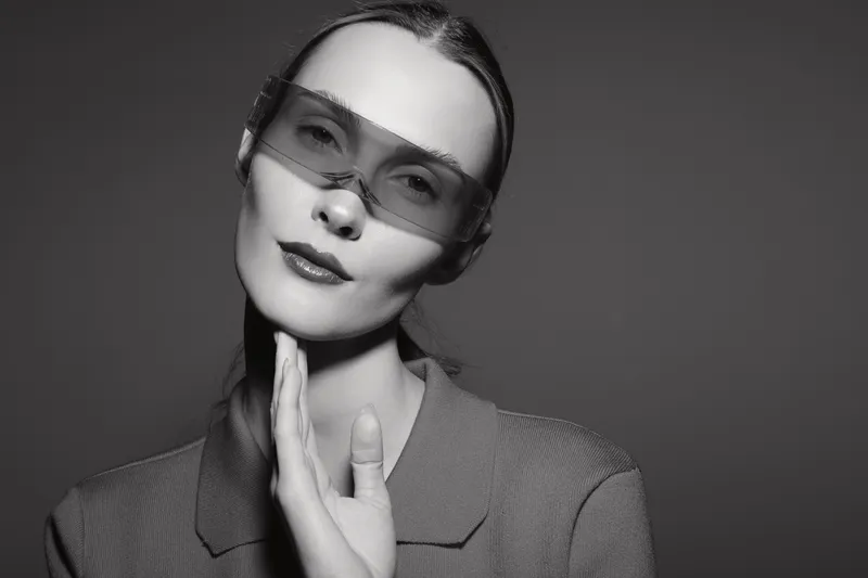 Portrait of a fair skinned white woman with slicked back hair wearing sunglasses and a blazer posing with hand near face in studio. Concept of fashion and style.