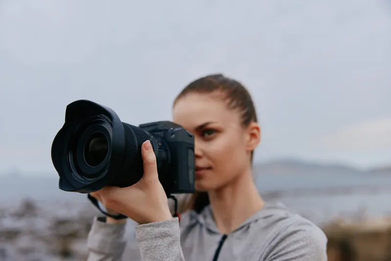 Young woman with a camera capturing outdoor scenery, showcasing creativity and passion for photography in a cloudy environment