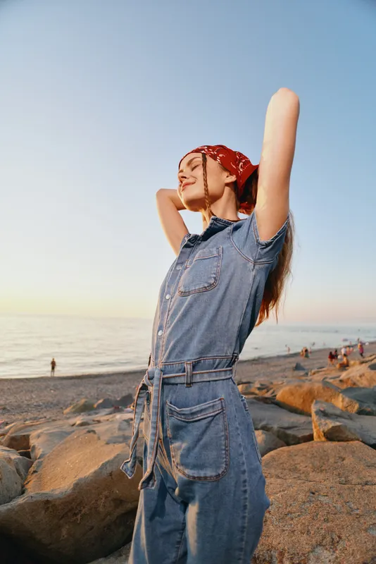 lifestyle woman in modern boho-western denim street style enjoying sunset by the beach with film color effects, relaxed and carefree mood in warm light.