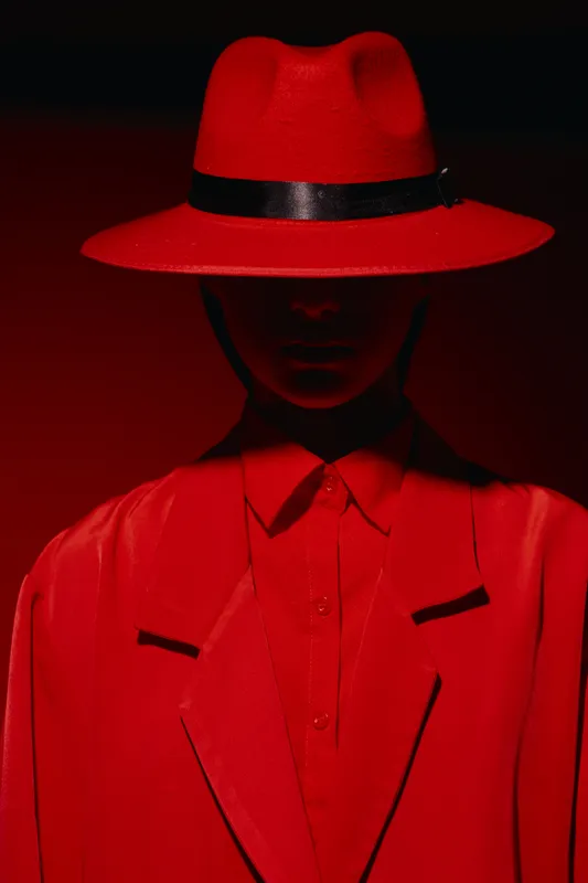 Silent female portrait in bright red hat, blazer and shirt in dramatic moody lighting against black background. Concept of bold fashion and creative beauty.
