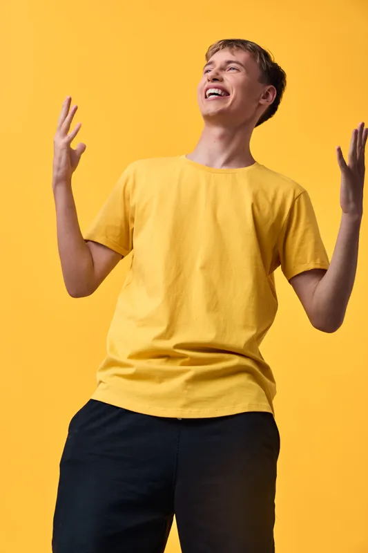 Joyful young man in a yellow t shirt raises hands in celebration, radiating energy and happiness with casual street style, dynamic pose, vivid backdrop and expressive mood for lifestyle imagery,