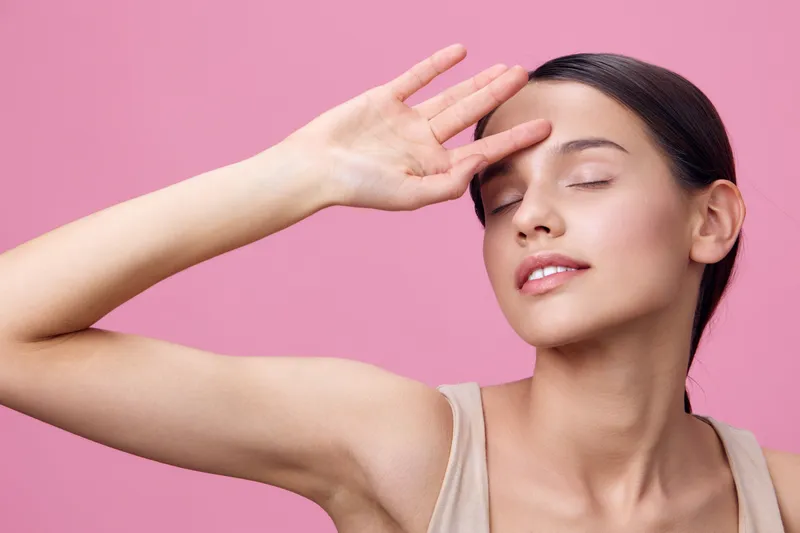 A serene young woman with an expressive pose, wearing a beige top against a soft pink background, conveying a sense of calmness and emotion