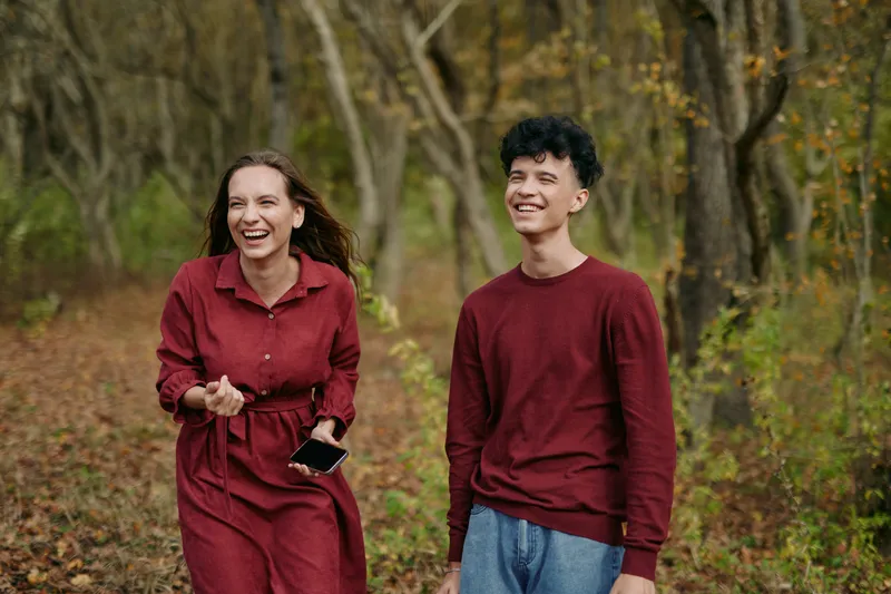 A candid moment as two friends walk through an autumn forest, smiling and relaxed, capturing genuine connection and authentic joy outdoors in warm natural light, together.