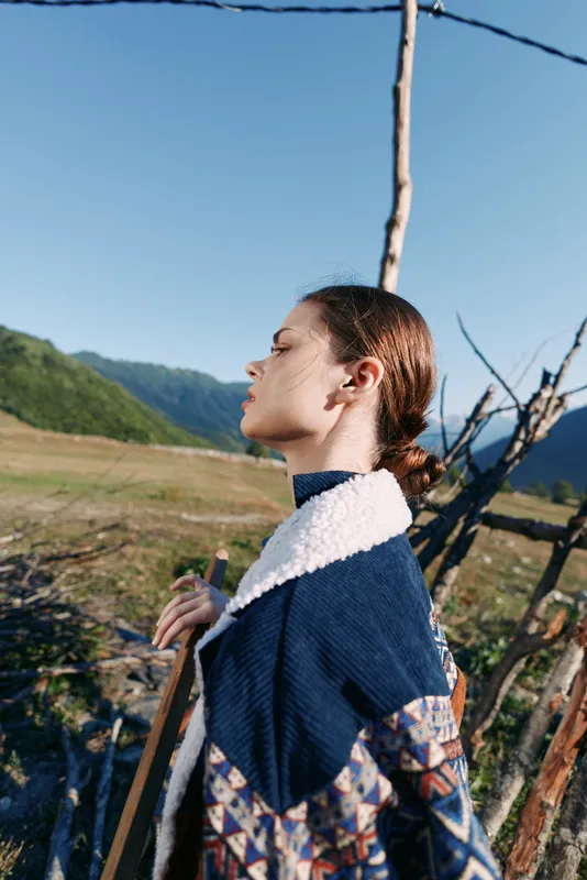 Woman profile portrait in countryside with mountains and wooden fence, hiking with a staff. Nature scene captures a thoughtful female outdoors, peaceful rustic landscape and travel vibe.