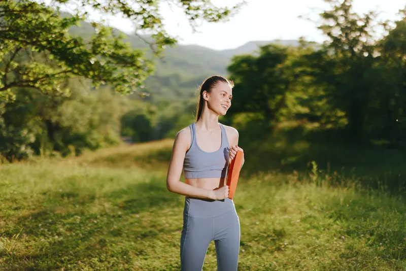 Young athletic woman in sportswear enjoying outdoor exercise in nature, holding weights, expressing joy and determination