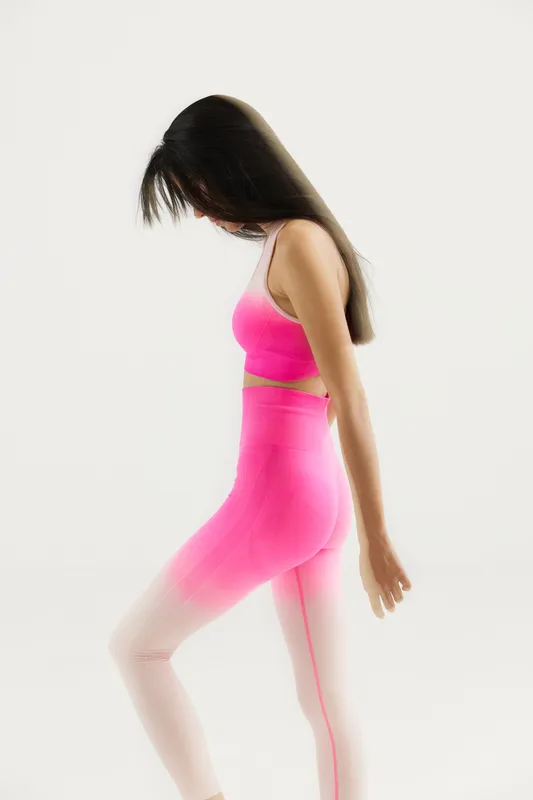 Woman sport fitness wearing bright pink activewear, standing in a minimalist white studio with natural light, displaying healthy lifestyle and strength.