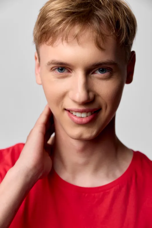 Smiling young man in a bright red shirt poses casually with a relaxed posture and friendly gaze, ideal for lifestyle, fashion, and wellness visuals