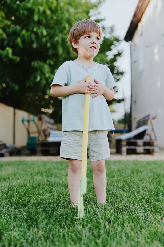 Playful boy standing with a yellow shovel, enjoying outdoor activities in a bright, green garden. Perfect for themes of childhood and exploration.