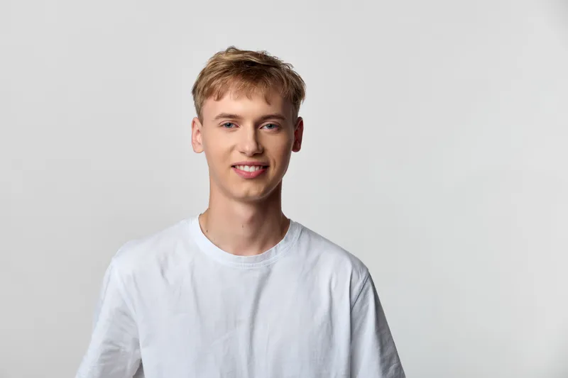 Smile, young man, white tee, casual wear in studio shot with cheerful expression against a clean background, creating an approachable headshot suitable for fashion, lifestyle, or corporate branding