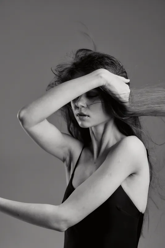 Black and white portrait of a young woman in motion with flowing hair and expressive gesture, conveying elegance and emotion.