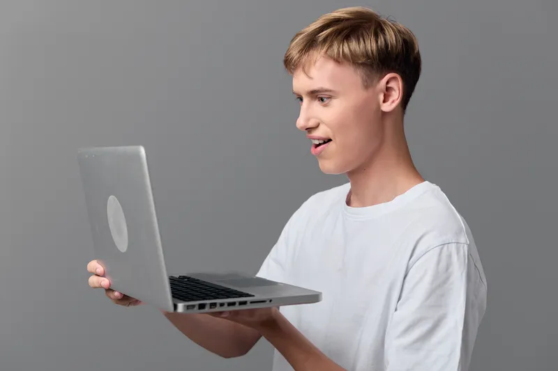Man with laptop held at chest level, casual white tee, smiling while viewing the screen, technology in use, online learning and remote work concept, modern device demonstration