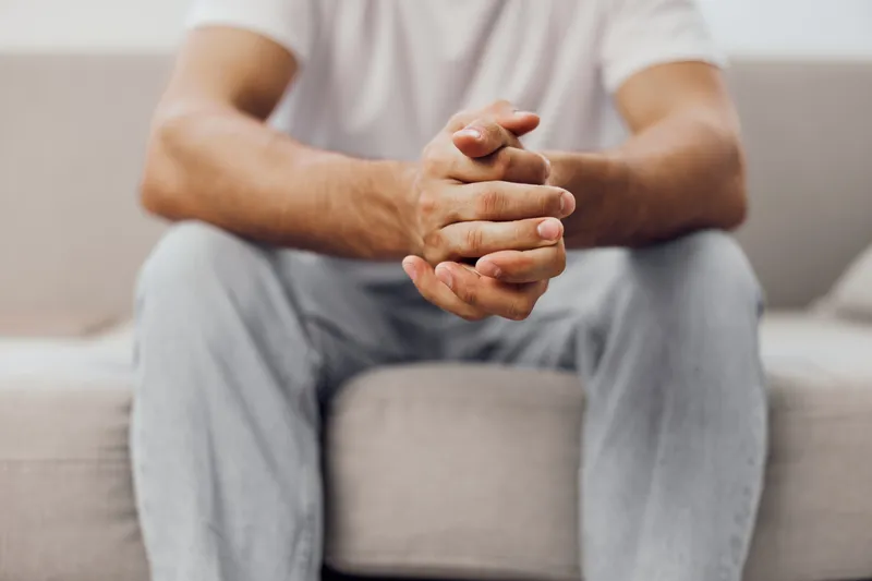 Thoughtful man sitting on a couch, resting his hands together. Modern interior setting with soft colors, representing relaxation and contemplation.
