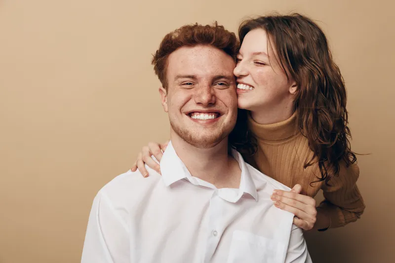 Happy young couple in casual clothes smiling and embracing each other on beige background. Concept of love, friendship, relationship, and positive emotions between people.